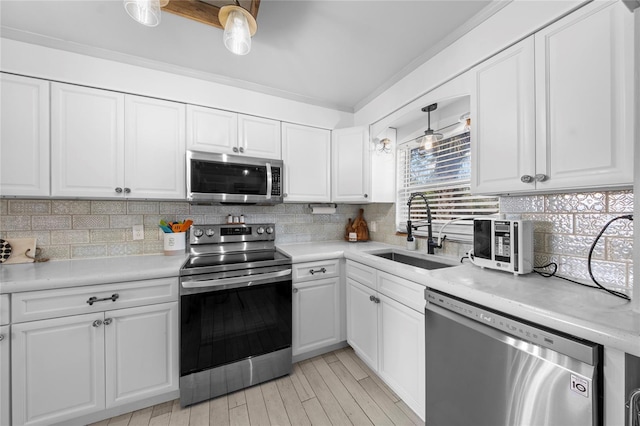 kitchen featuring pendant lighting, white cabinets, appliances with stainless steel finishes, decorative backsplash, and sink