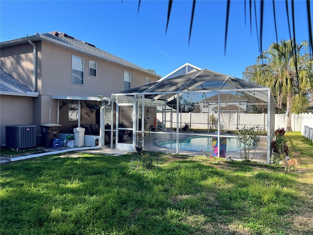 rear view of property with a patio, a lanai, a yard, central air condition unit, and a fenced in pool