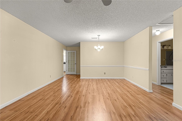 spare room with a textured ceiling, light hardwood / wood-style floors, a notable chandelier, and sink