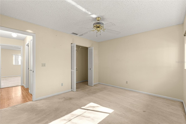 unfurnished bedroom featuring ceiling fan, a textured ceiling, a closet, and light carpet