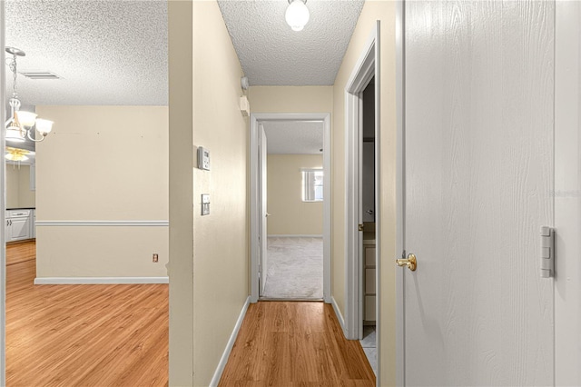 hall with a textured ceiling, light hardwood / wood-style flooring, and a notable chandelier