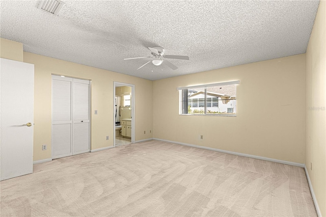 unfurnished bedroom with light carpet, ceiling fan, a textured ceiling, and connected bathroom