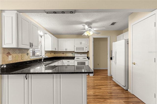 kitchen featuring white cabinetry, kitchen peninsula, white appliances, dark stone countertops, and sink