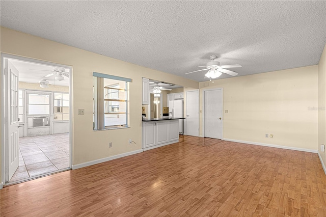 unfurnished living room with ceiling fan, a textured ceiling, and light wood-type flooring