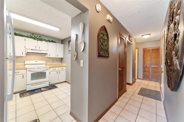 kitchen with refrigerator, white range with electric stovetop, light tile patterned floors, a textured ceiling, and white cabinets