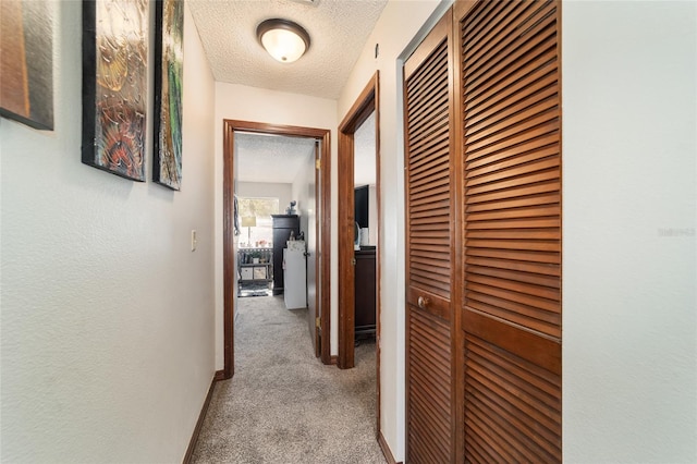 hallway with a textured ceiling and light colored carpet