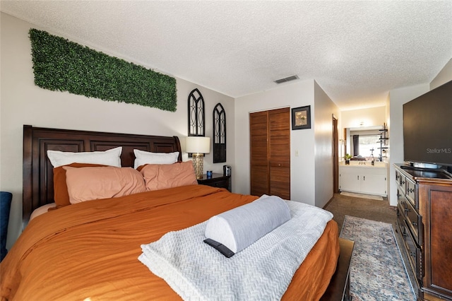 carpeted bedroom featuring a textured ceiling, ensuite bathroom, and a closet