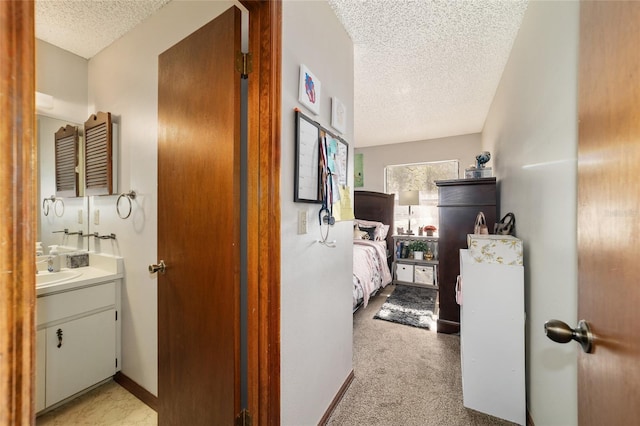 hall with a textured ceiling, light colored carpet, and sink