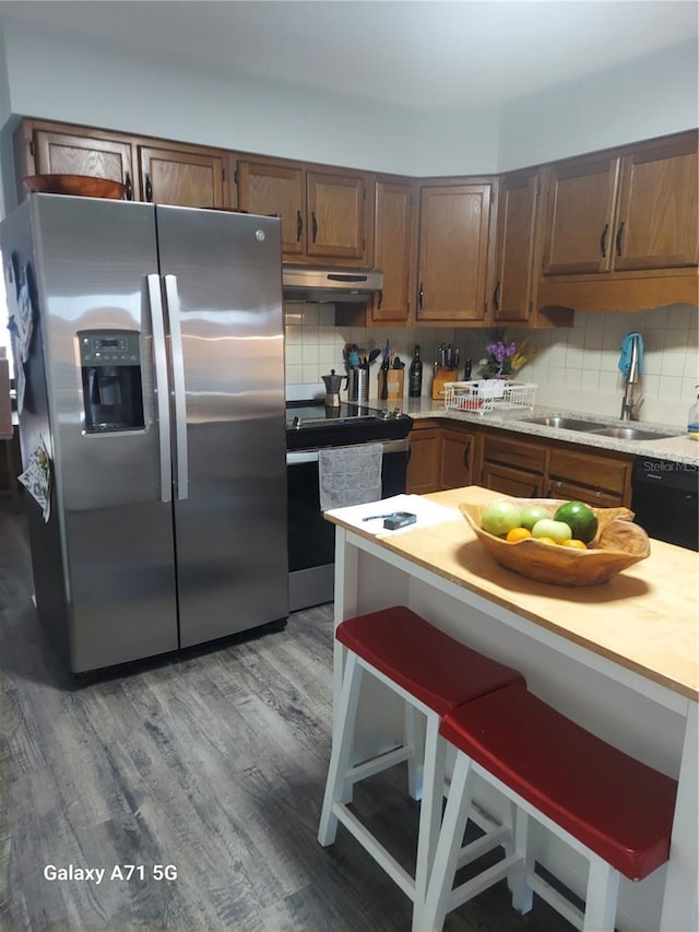 kitchen with wood-type flooring, stainless steel appliances, sink, backsplash, and a breakfast bar