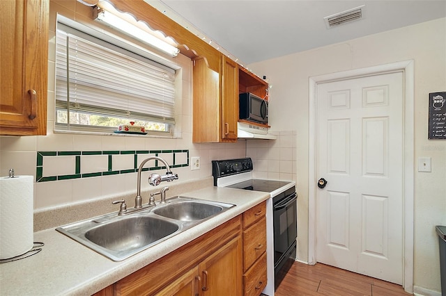 kitchen with black appliances, decorative backsplash, sink, and light hardwood / wood-style flooring