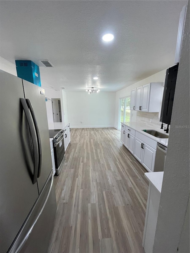 kitchen with sink, appliances with stainless steel finishes, white cabinetry, backsplash, and a textured ceiling