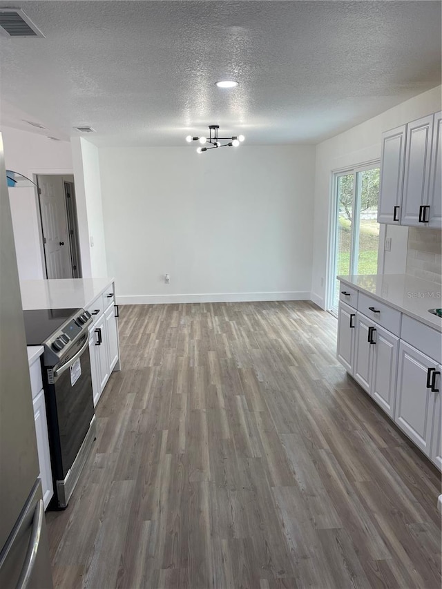 kitchen with white cabinetry, hardwood / wood-style floors, a notable chandelier, a textured ceiling, and stainless steel range with electric cooktop