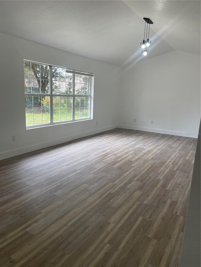 spare room featuring dark wood-type flooring, vaulted ceiling, and a textured ceiling