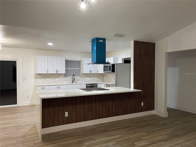 kitchen with appliances with stainless steel finishes, hardwood / wood-style floors, island range hood, sink, and white cabinets