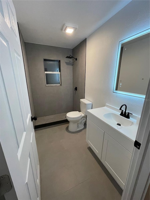 bathroom featuring a tile shower, vanity, and toilet