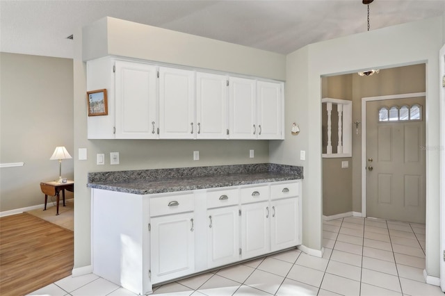 kitchen featuring dark countertops, white cabinets, light tile patterned floors, and baseboards