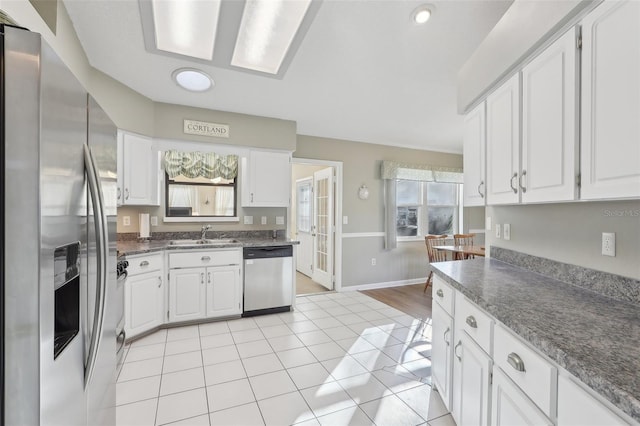 kitchen with a sink, white cabinetry, stainless steel appliances, light tile patterned floors, and baseboards