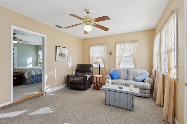 living room with ceiling fan, visible vents, baseboards, and light carpet