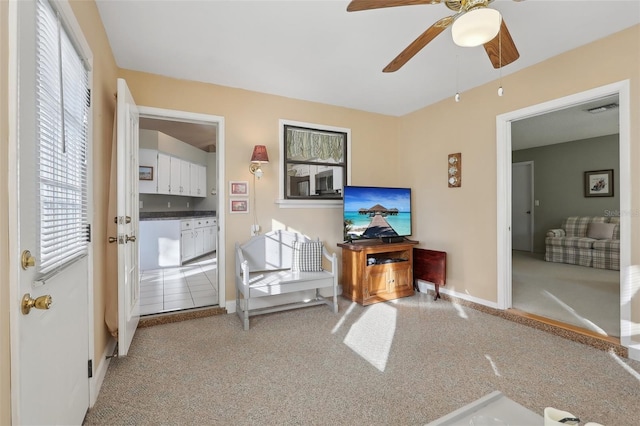 living area featuring visible vents, light colored carpet, baseboards, and ceiling fan