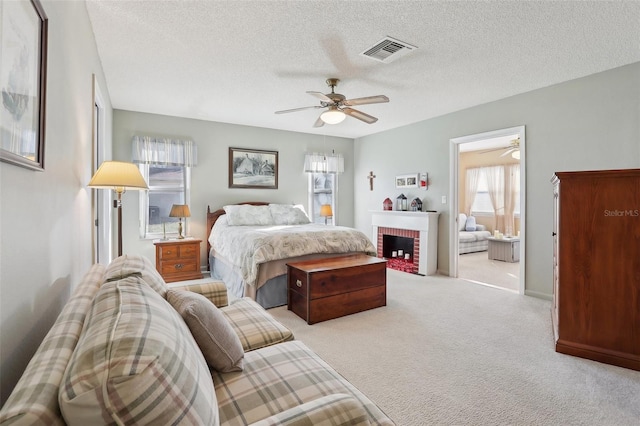 bedroom with visible vents, a textured ceiling, carpet floors, a fireplace, and ceiling fan