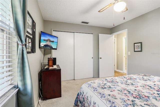 carpeted bedroom with ceiling fan, visible vents, a closet, and a textured ceiling