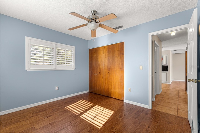 unfurnished bedroom with a closet, ceiling fan, a textured ceiling, and dark hardwood / wood-style flooring