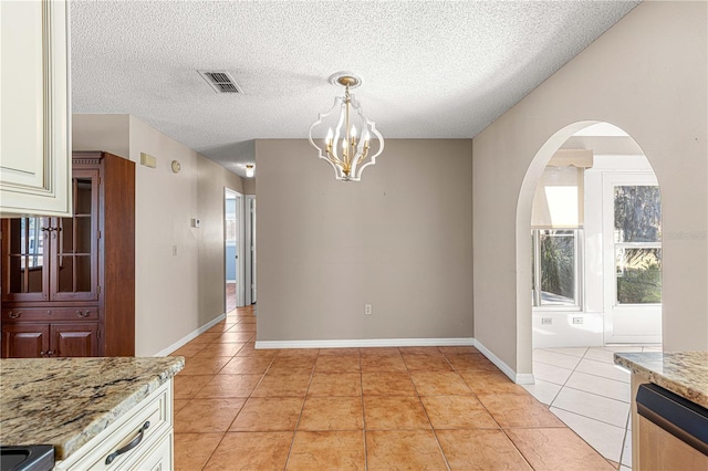 unfurnished dining area featuring a textured ceiling, an inviting chandelier, and light tile patterned flooring