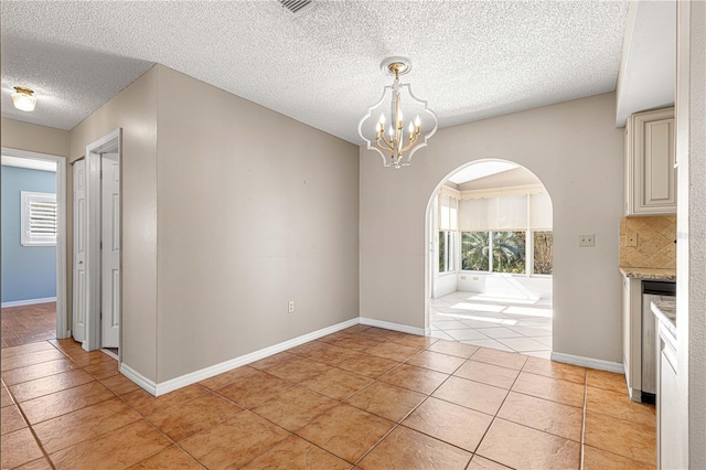 unfurnished dining area with a textured ceiling, light tile patterned floors, and an inviting chandelier