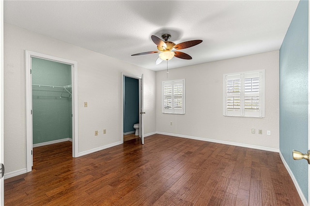 unfurnished bedroom featuring ceiling fan, ensuite bathroom, dark hardwood / wood-style flooring, a spacious closet, and a closet