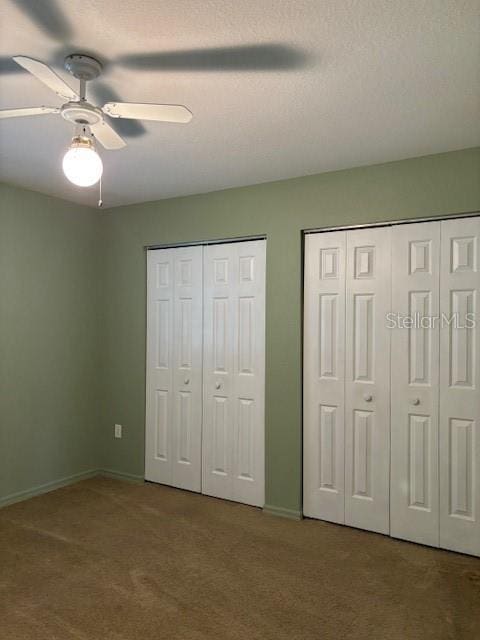 unfurnished bedroom featuring ceiling fan, carpet flooring, and two closets