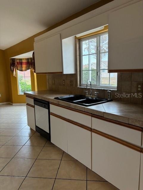 kitchen with light tile patterned flooring, sink, dishwasher, white cabinets, and backsplash