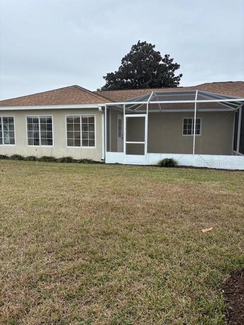 back of property with a yard and glass enclosure