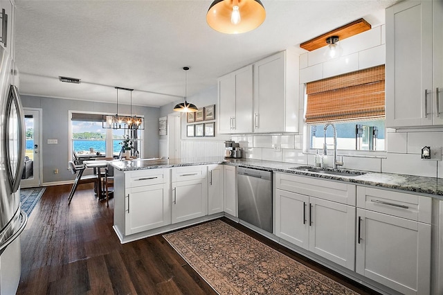 kitchen with kitchen peninsula, appliances with stainless steel finishes, decorative light fixtures, white cabinets, and sink