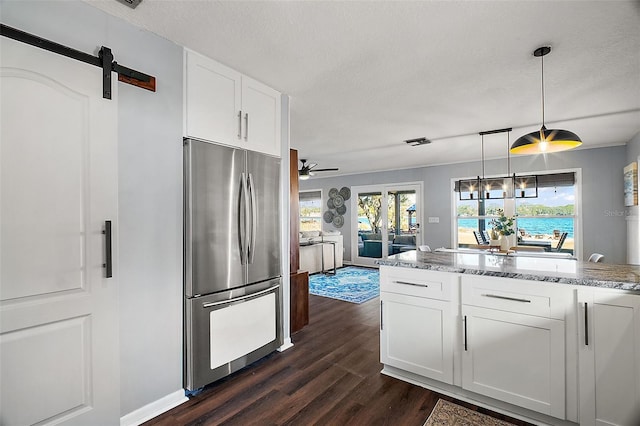 kitchen featuring a barn door, pendant lighting, stainless steel refrigerator, white cabinetry, and light stone countertops