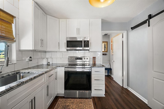 kitchen with appliances with stainless steel finishes, dark stone countertops, a barn door, and white cabinetry