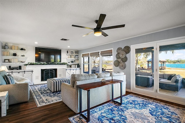 living room with ceiling fan, a fireplace, hardwood / wood-style flooring, ornamental molding, and a textured ceiling