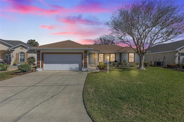 ranch-style home with a garage, a yard, and central AC unit