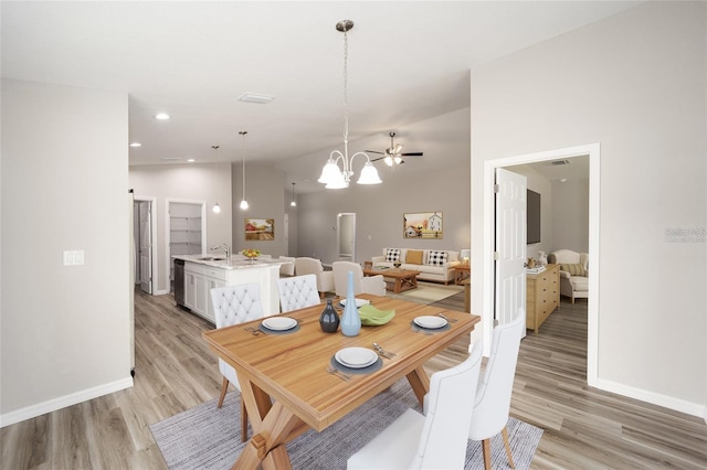 dining room with sink, light hardwood / wood-style flooring, vaulted ceiling, and a notable chandelier