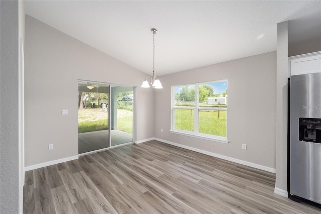 unfurnished dining area with a notable chandelier, vaulted ceiling, and light hardwood / wood-style floors