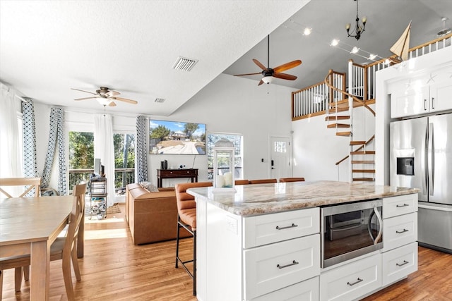 kitchen with a kitchen island, appliances with stainless steel finishes, white cabinets, and light stone counters