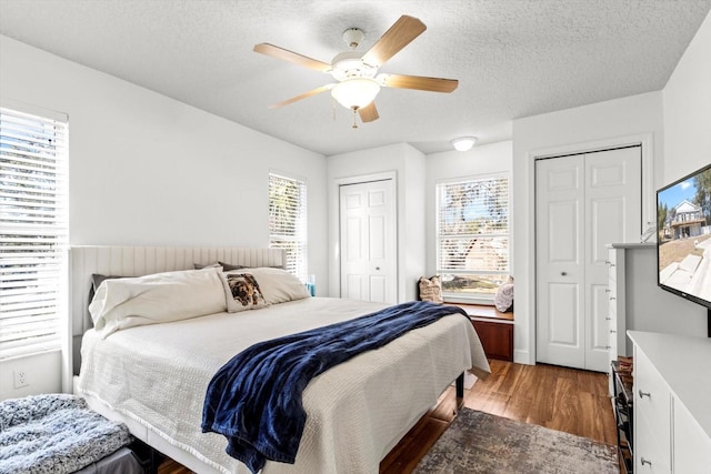 bedroom featuring a textured ceiling, a ceiling fan, multiple closets, and wood finished floors