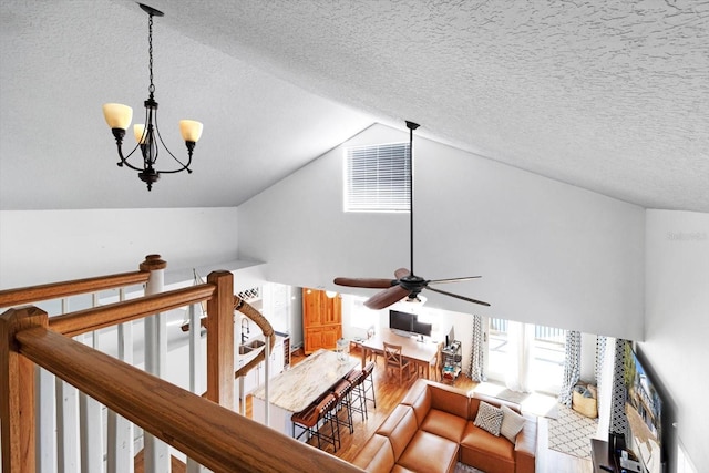 living room featuring ceiling fan with notable chandelier, lofted ceiling, a textured ceiling, and wood finished floors