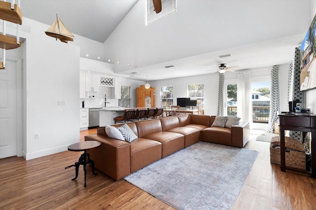 living room featuring ceiling fan, a towering ceiling, and light hardwood / wood-style floors