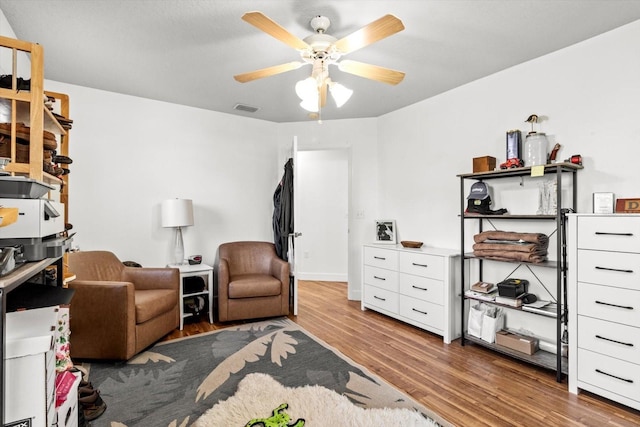 living area with wood finished floors, visible vents, and a ceiling fan