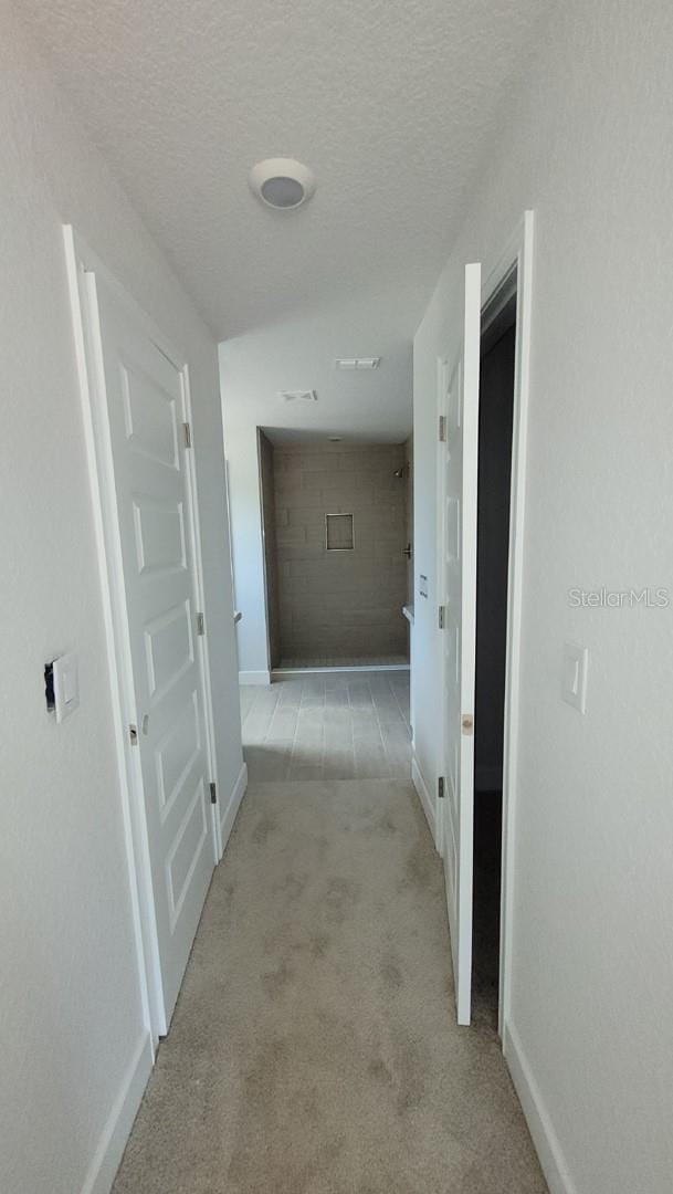 corridor featuring light colored carpet and a textured ceiling