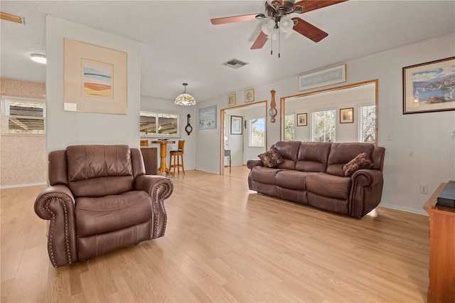 living room featuring ceiling fan, a textured ceiling, and light wood-type flooring