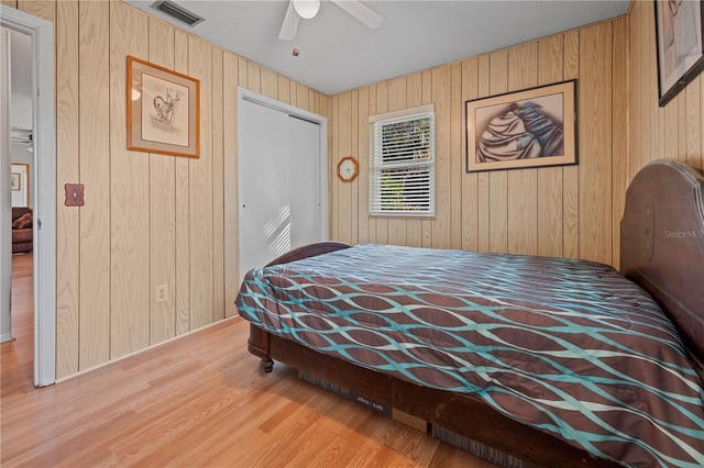 bedroom with ceiling fan, a closet, wood walls, and light hardwood / wood-style flooring