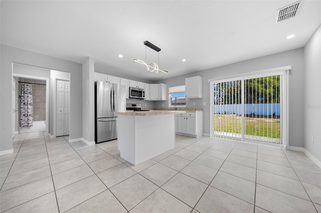 kitchen with white cabinetry, stainless steel appliances, light stone countertops, a kitchen island, and pendant lighting