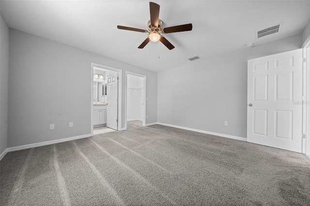 unfurnished bedroom with ceiling fan, ensuite bath, a closet, light colored carpet, and a walk in closet