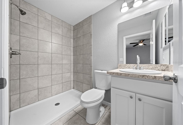 bathroom with tile patterned floors, vanity, toilet, ceiling fan, and tiled shower